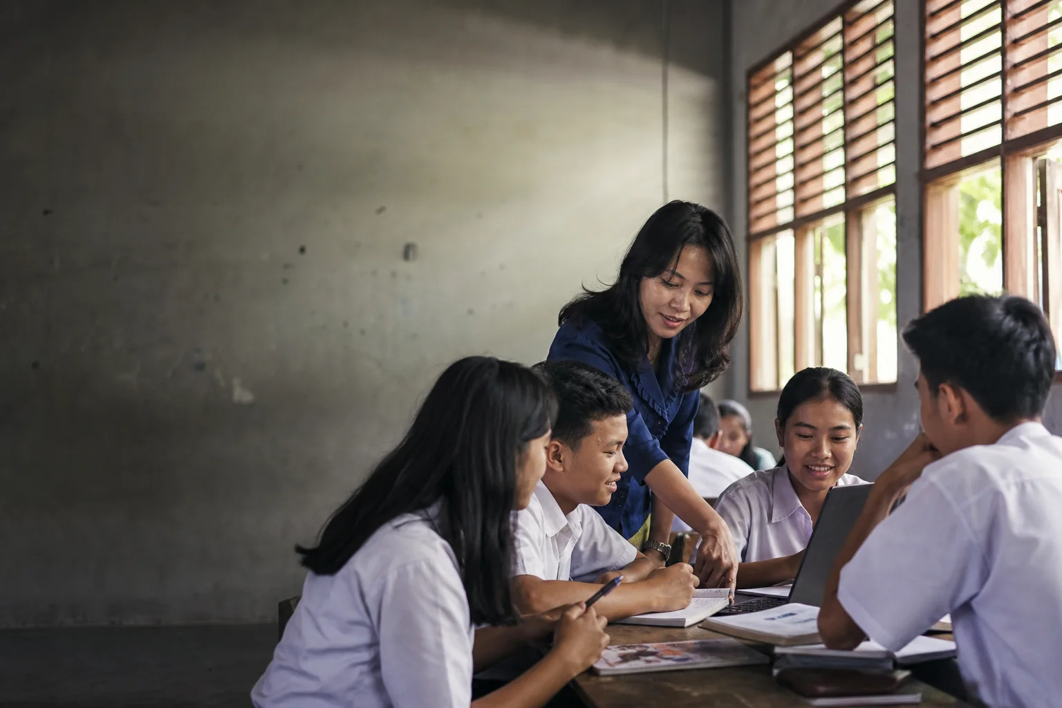 Guru mendampingi siswa berdiskusi dan belajar dengan laptop di ruang kelas